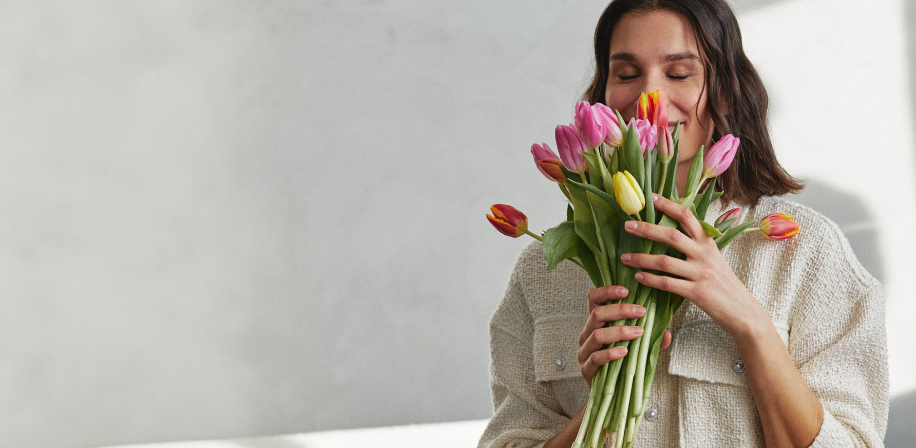 Ein weißer, kuscheliger Pullover umhüllt sanft die Person, die bunte Tulpen hält.