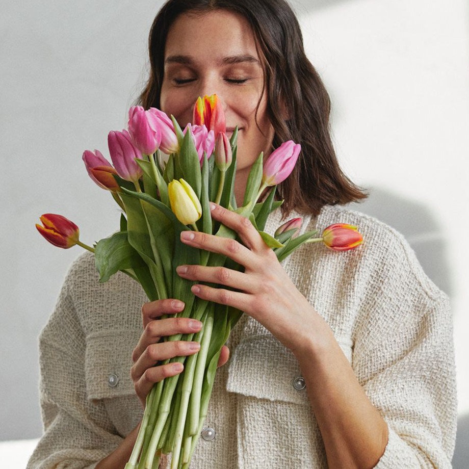 Ein weißer, kuscheliger Pullover umhüllt sanft die Person, die bunte Tulpen hält.