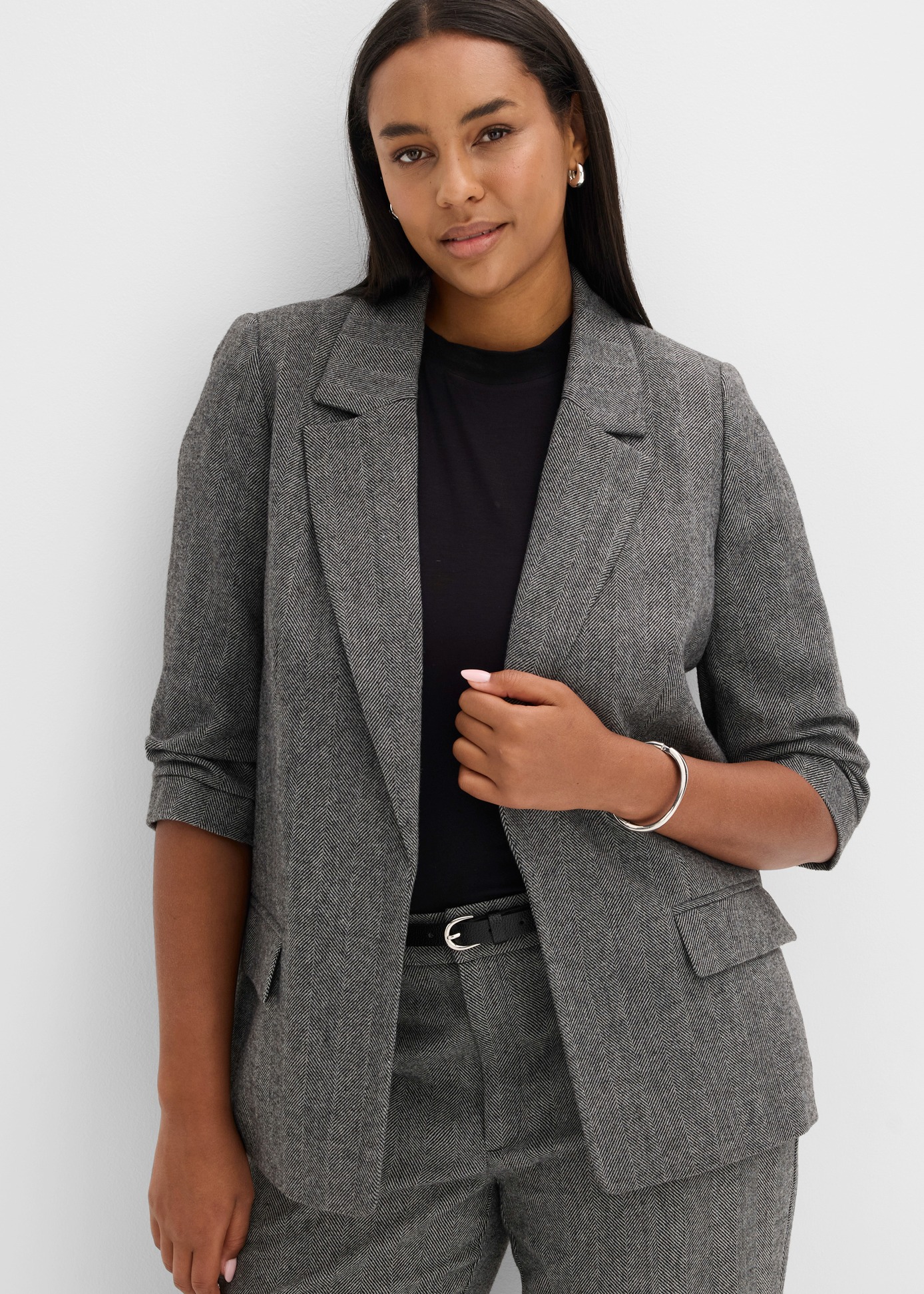 Elegantes Ensemble: Grauer gemusterter Blazer, schwarzes Top, passende Hose und schicker Gürtel.