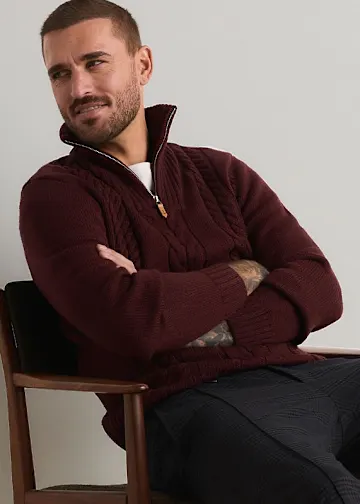 Dunkelroter Zopfstrickpullover mit Reißverschluss und gemusterter Hose bilden ein stilvolles Outfit.