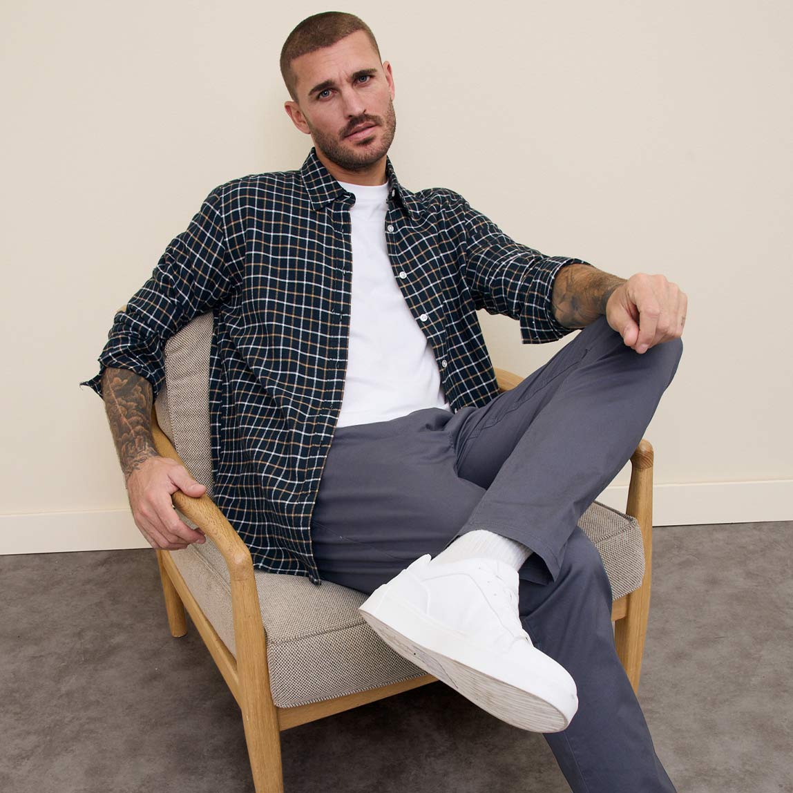 Kariertes Hemd über weißem T-Shirt, graue Hose und weiße Sneaker. Lässiger, moderner Look.