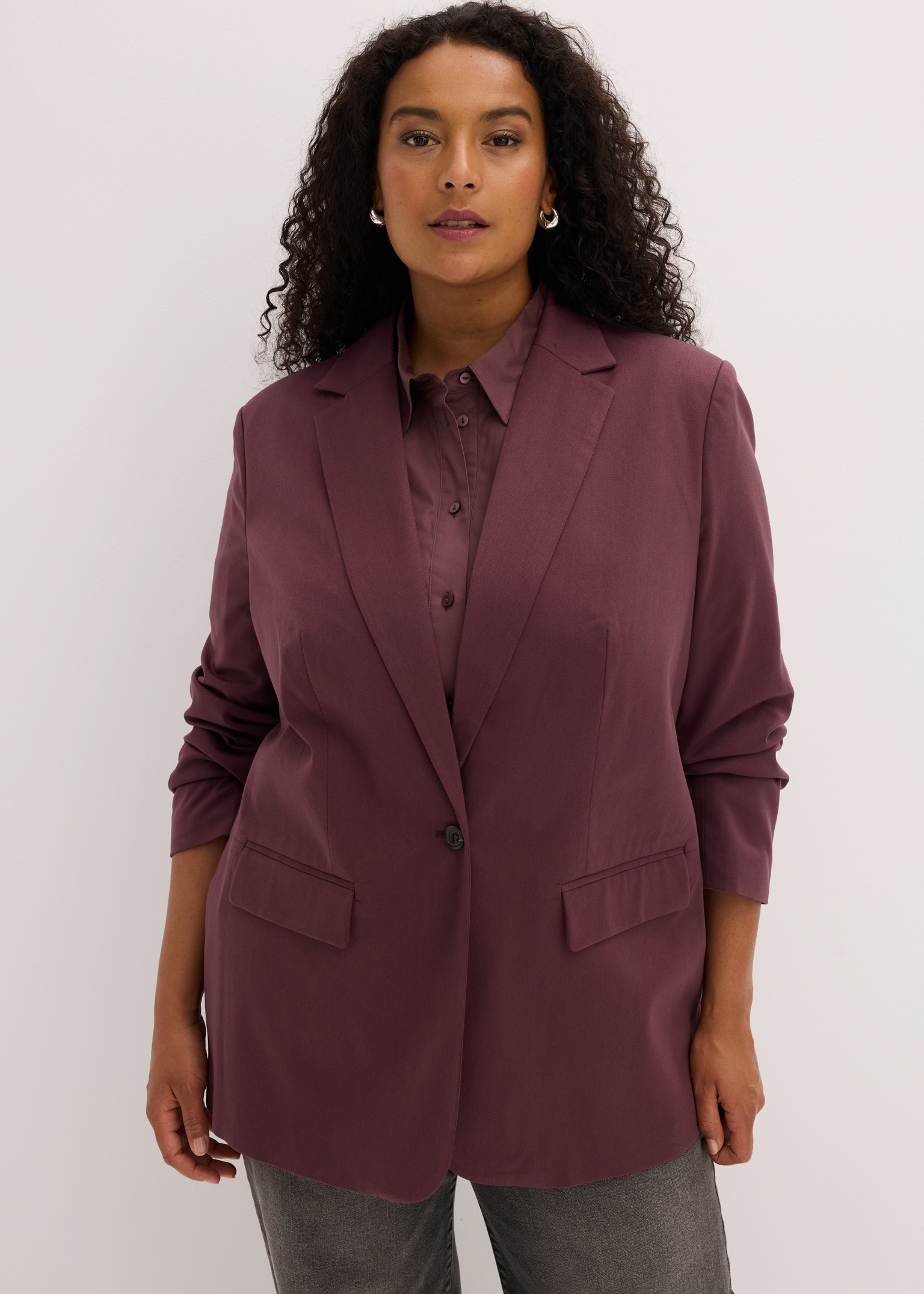 Modischer pflaumenfarbener Blazer mit passendem Hemd, kombiniert mit grauen Jeans.
