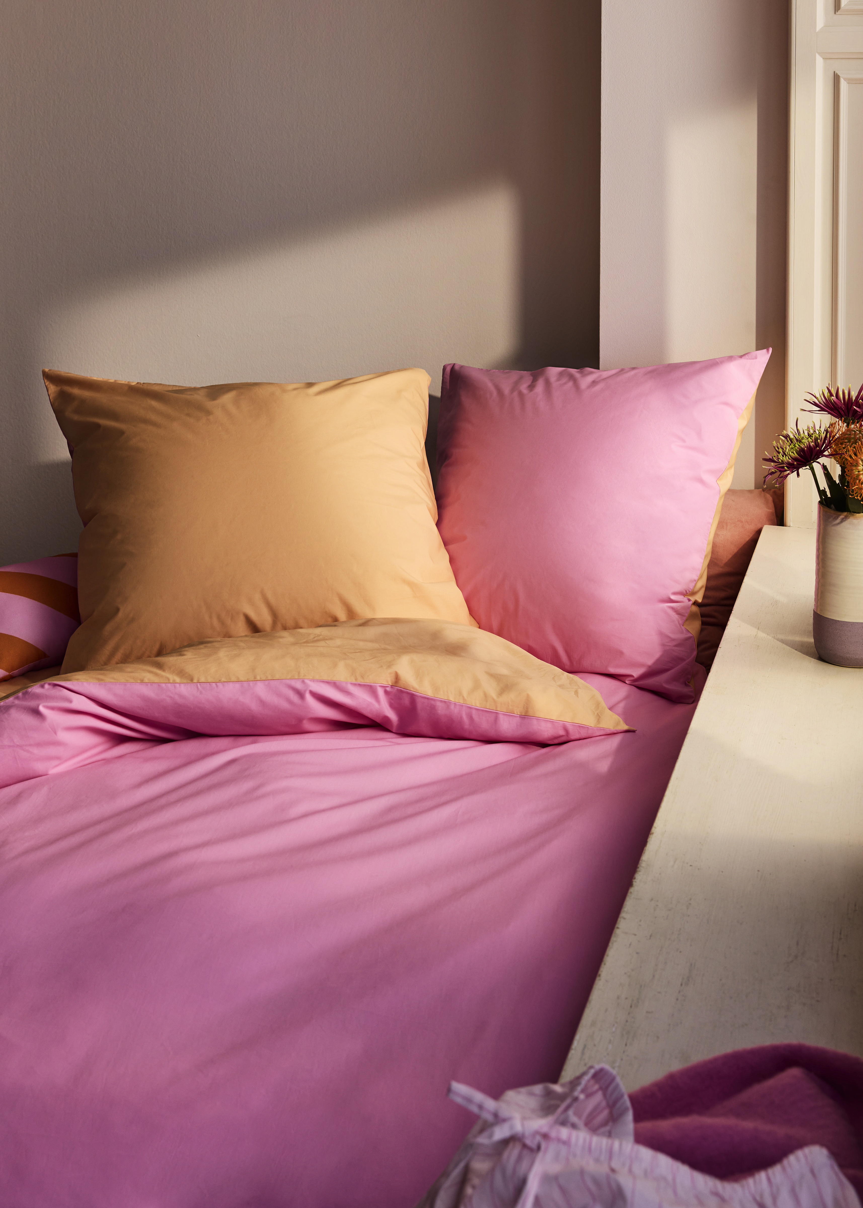 Leuchtend pinke und orangefarbene Textilien dominieren das gemütliche Schlafzimmerambiente.
