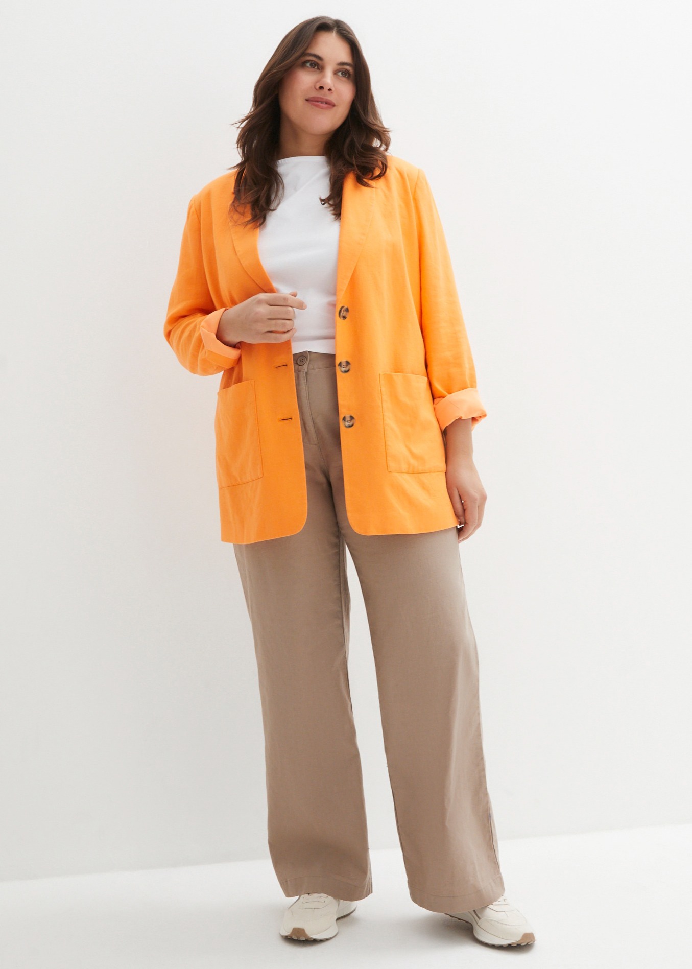 Orangefarbener Cardigan über weißem Top, beige Hose und helle Schuhe.
