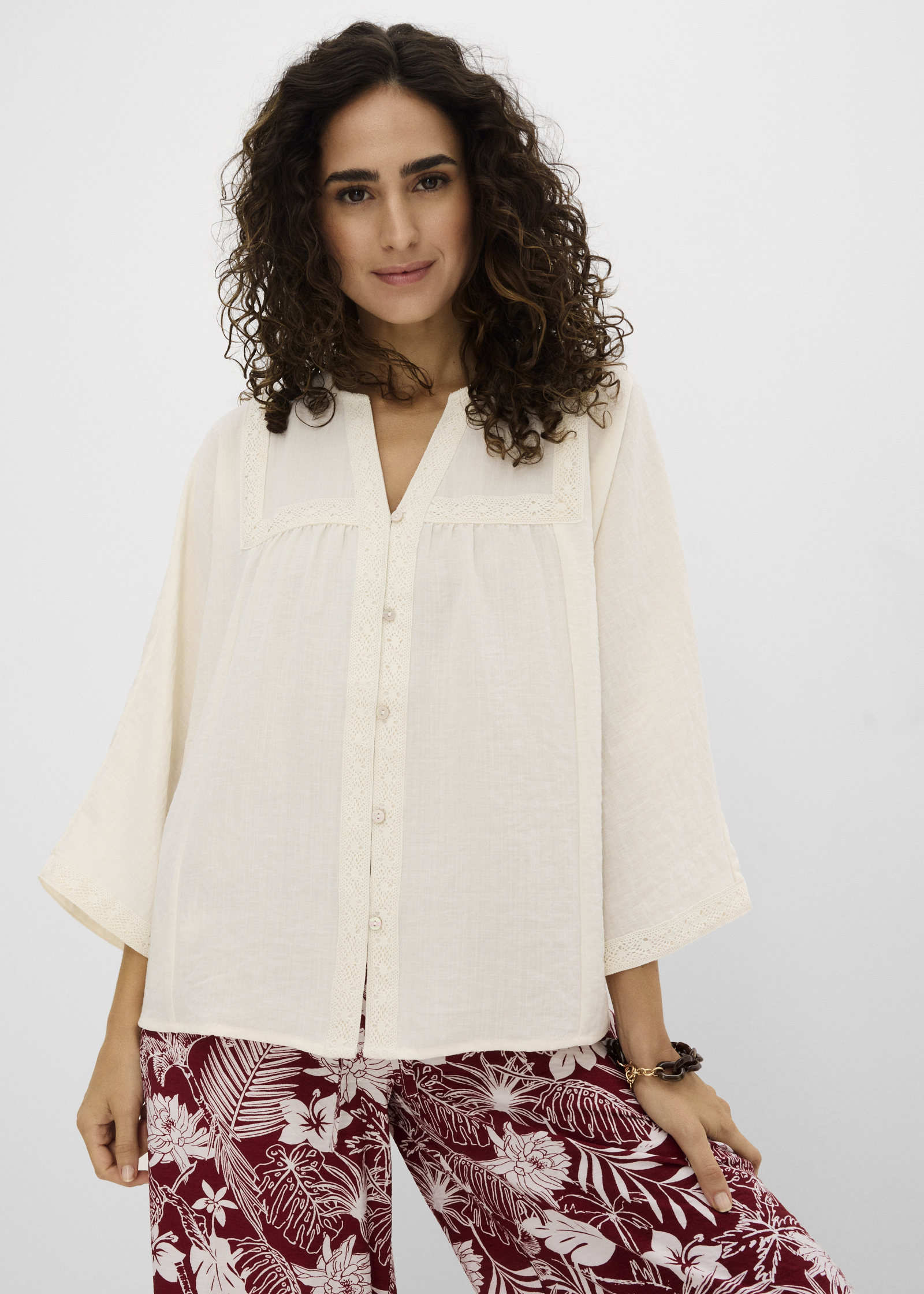 Elegante cremefarbene Bluse mit Spitze und weiten Ärmeln, dazu eine gemusterte Hose.
