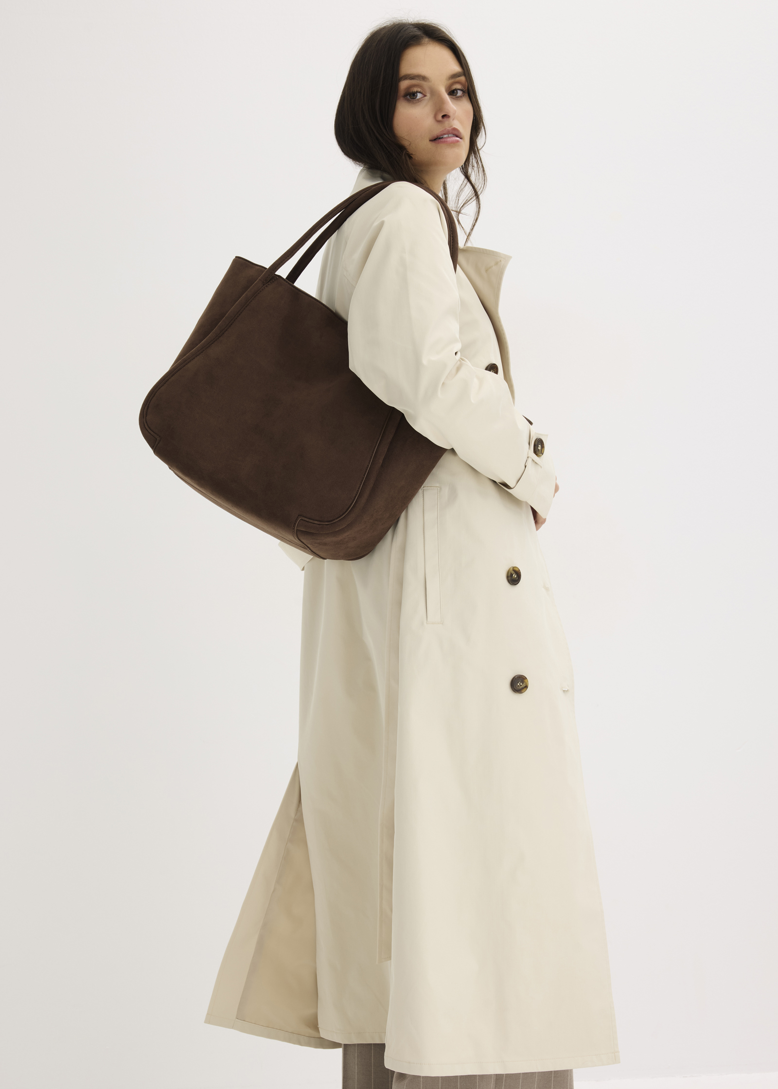 Sie trägt einen klassischen beigen Trenchcoat und eine große braune Tasche.