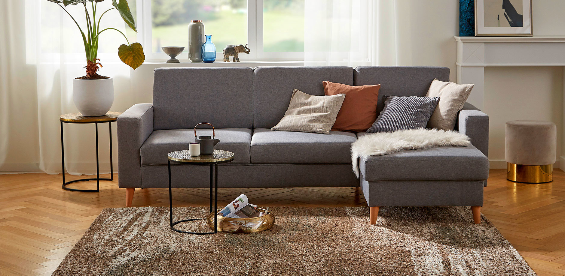 Graues Ecksofa mit braunen und weißen Kissen, perfekt für gemütliche Abende zuhause.