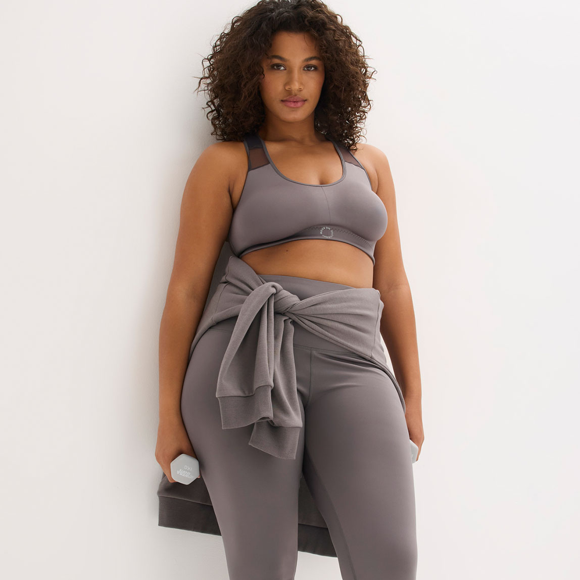 Graues Sport-Outfit mit Sport-BH und Leggings. Sweater um die Hüfte gebunden.