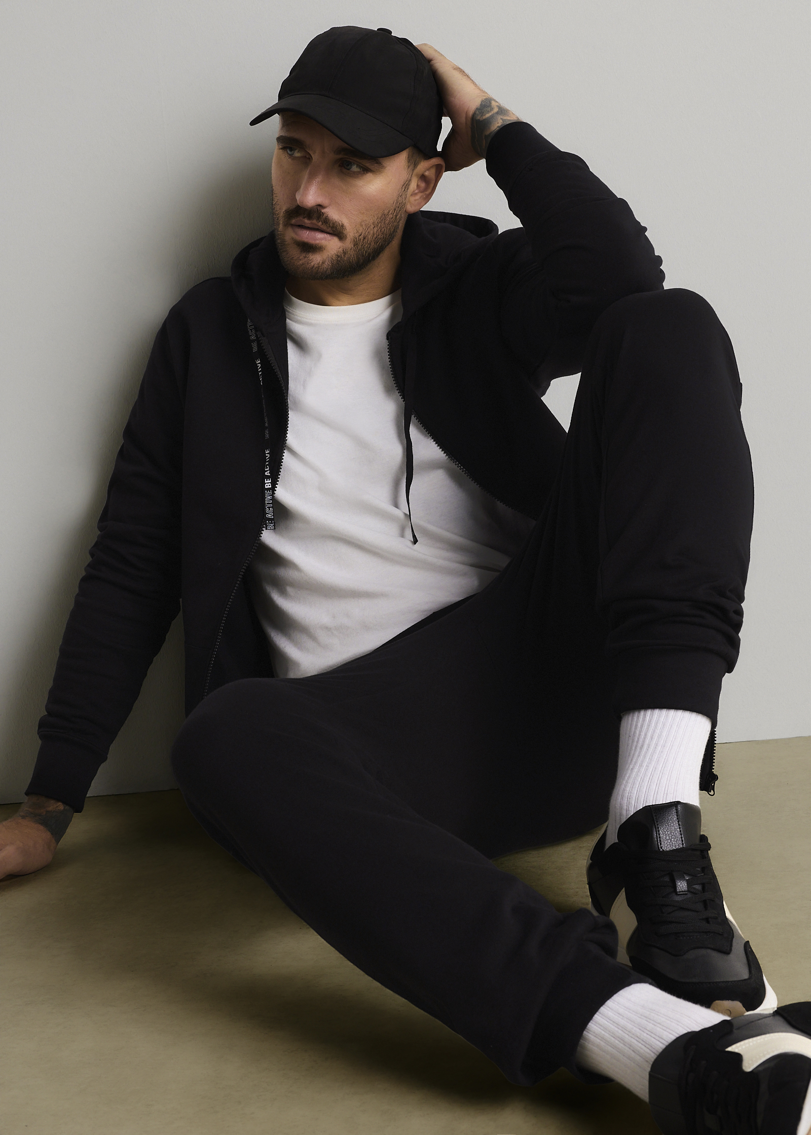 Schwarze Kappe, Kapuzenjacke, weißes T-Shirt, Jogginghose, weiße Socken und Turnschuhe.