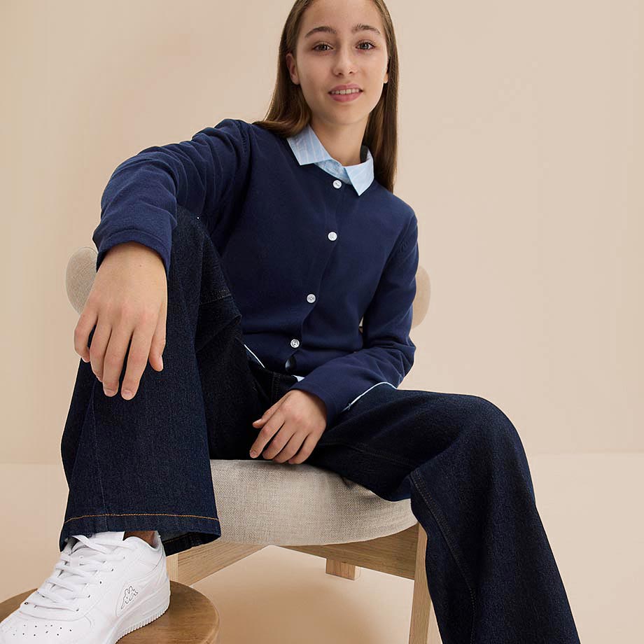 Dunkelblaue Jeans-Kombination mit weißem Kragen und Knöpfen, ergänzt durch weiße Turnschuhe.