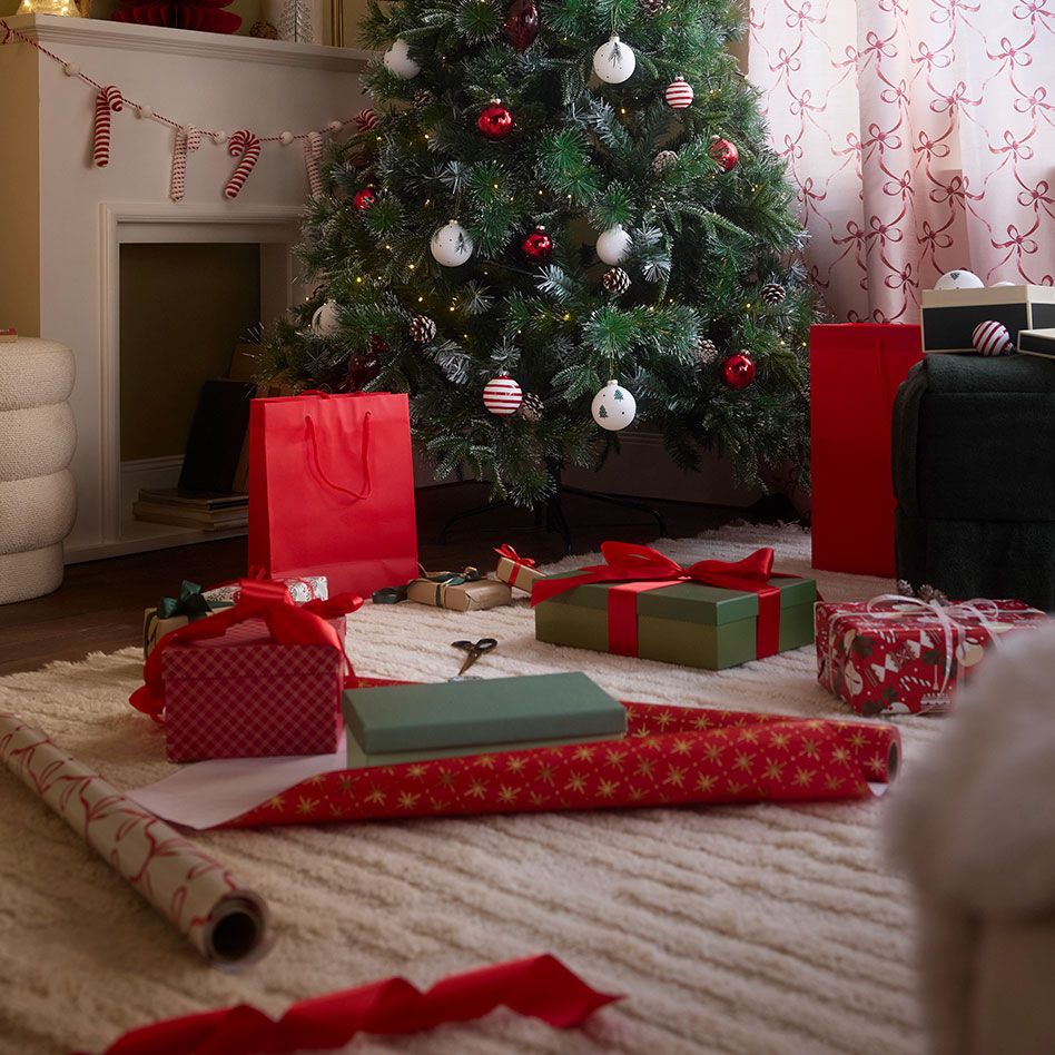 Verpackte Geschenke und Geschenkpapier liegen auf dem Teppich.