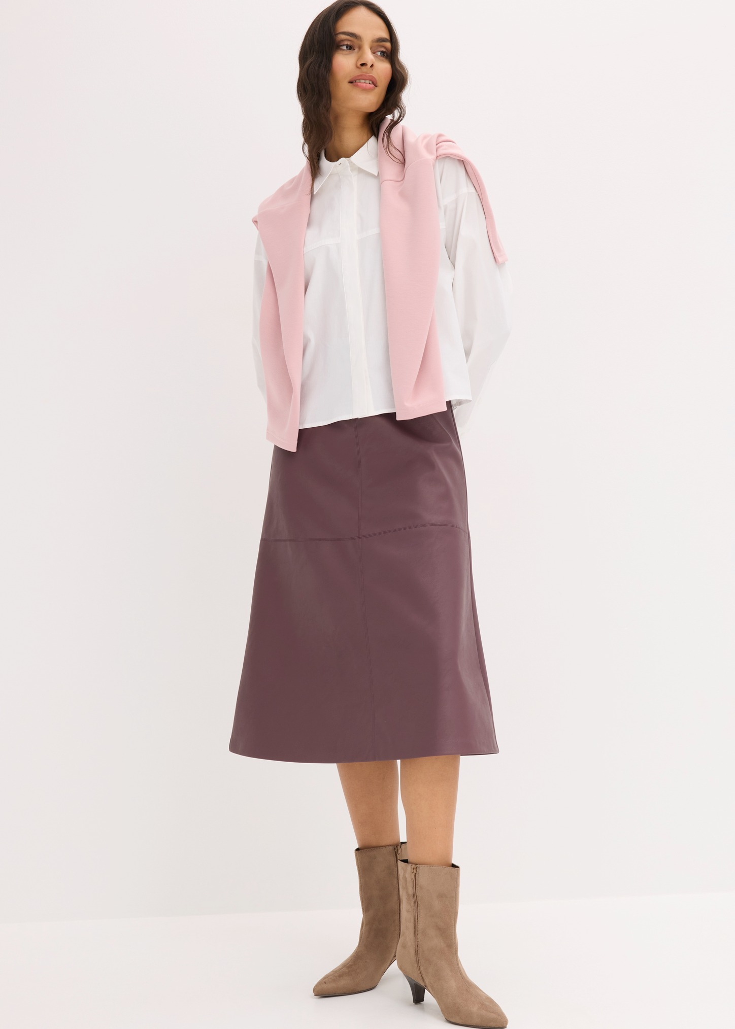 Weißes Hemd, rosa Pullover über den Schultern, pflaumenfarbener Rock und beige Stiefeletten.