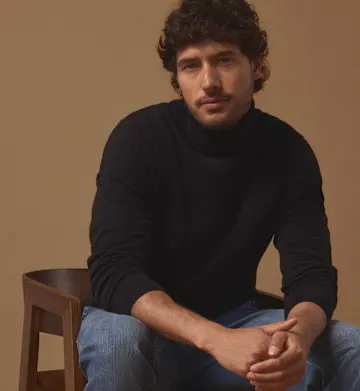Stilvoll in schwarzem Rollkragenpullover, blauer Jeans und dunklen Schnürstiefeln gekleidet.