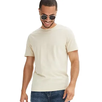 Er trägt ein einfaches, beiges T-Shirt und klassische blaue Jeans.