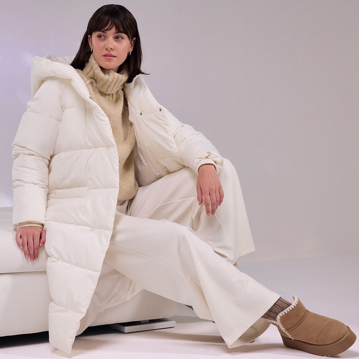 Cremefarbener Daunenmantel, weiße Hose und flauschige Boots.