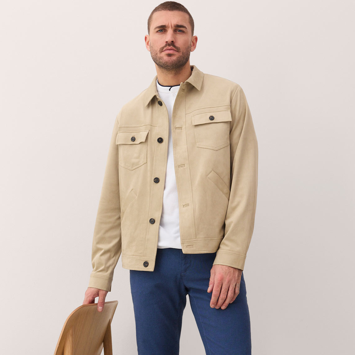 Mann trägt beige Hemdjacke mit Brusttaschen über weißem T-Shirt und blauen Jeans.