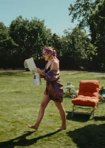 Frau läuft mit Zeitung in der Hand lesend durch den Garten.