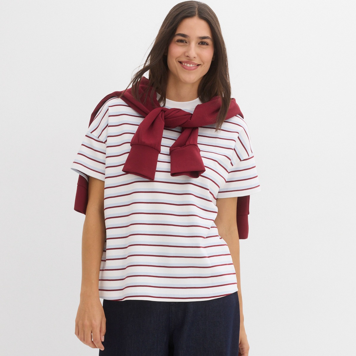 Gestreiftes T-Shirt und roter Pullover lässig um die Schultern gelegt. 