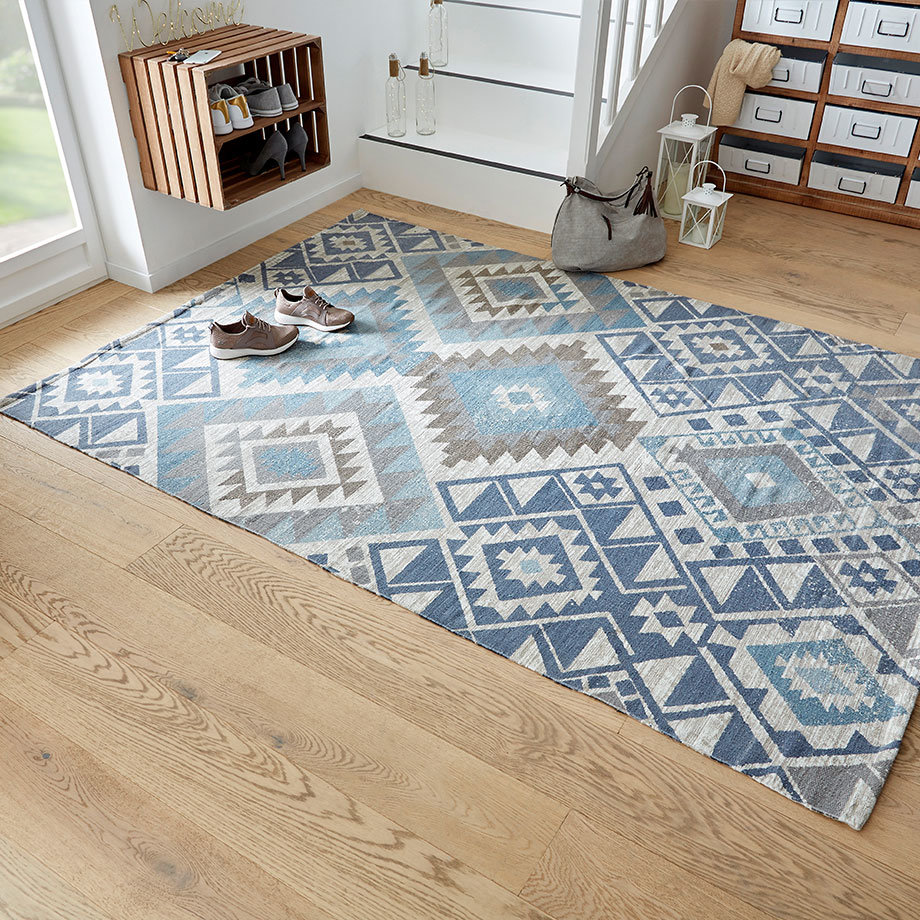 Ein gemusterter blau-weißer Teppich mit geometrischen Formen liegt auf hellem Holzboden im Eingangsbereich.