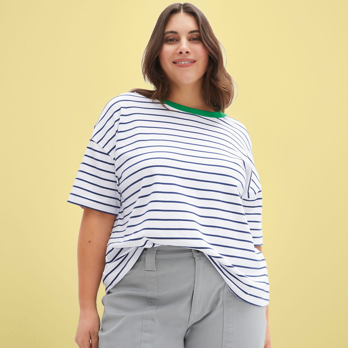 Frau trägt ein lockeres gestreiftes T-Shirt mit grünem Kragen und graue Hose.