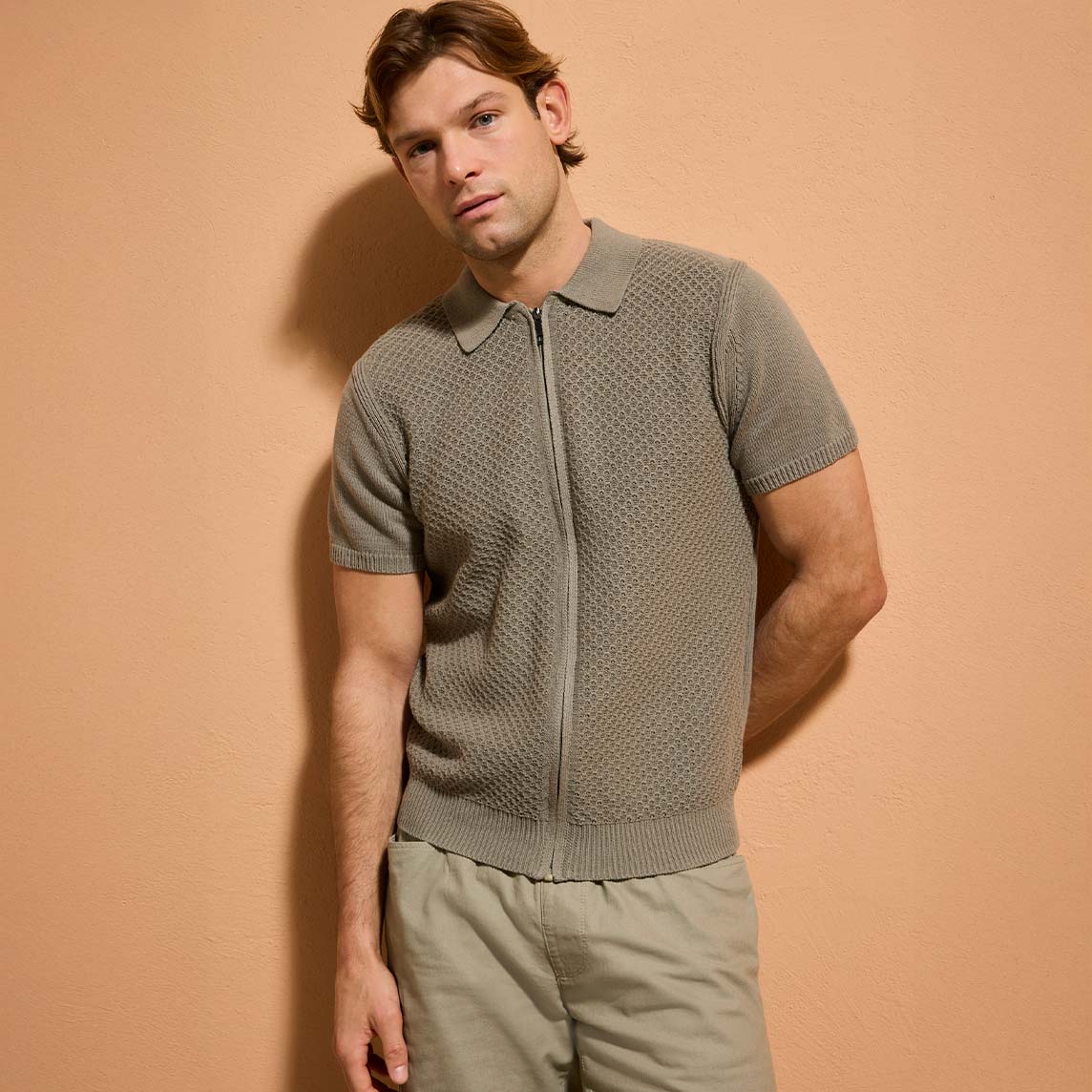 Grünes Poloshirt mit Reißverschluss und helle Hose.