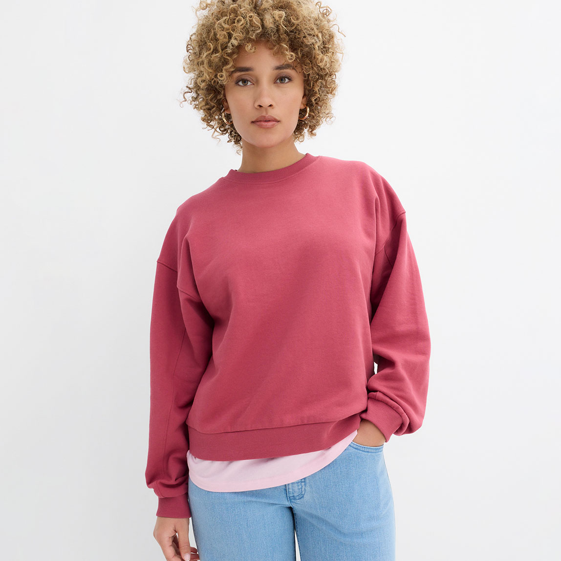 Rosa Sweatshirt und blaue Jeans im entspannten Streetwear-Look.