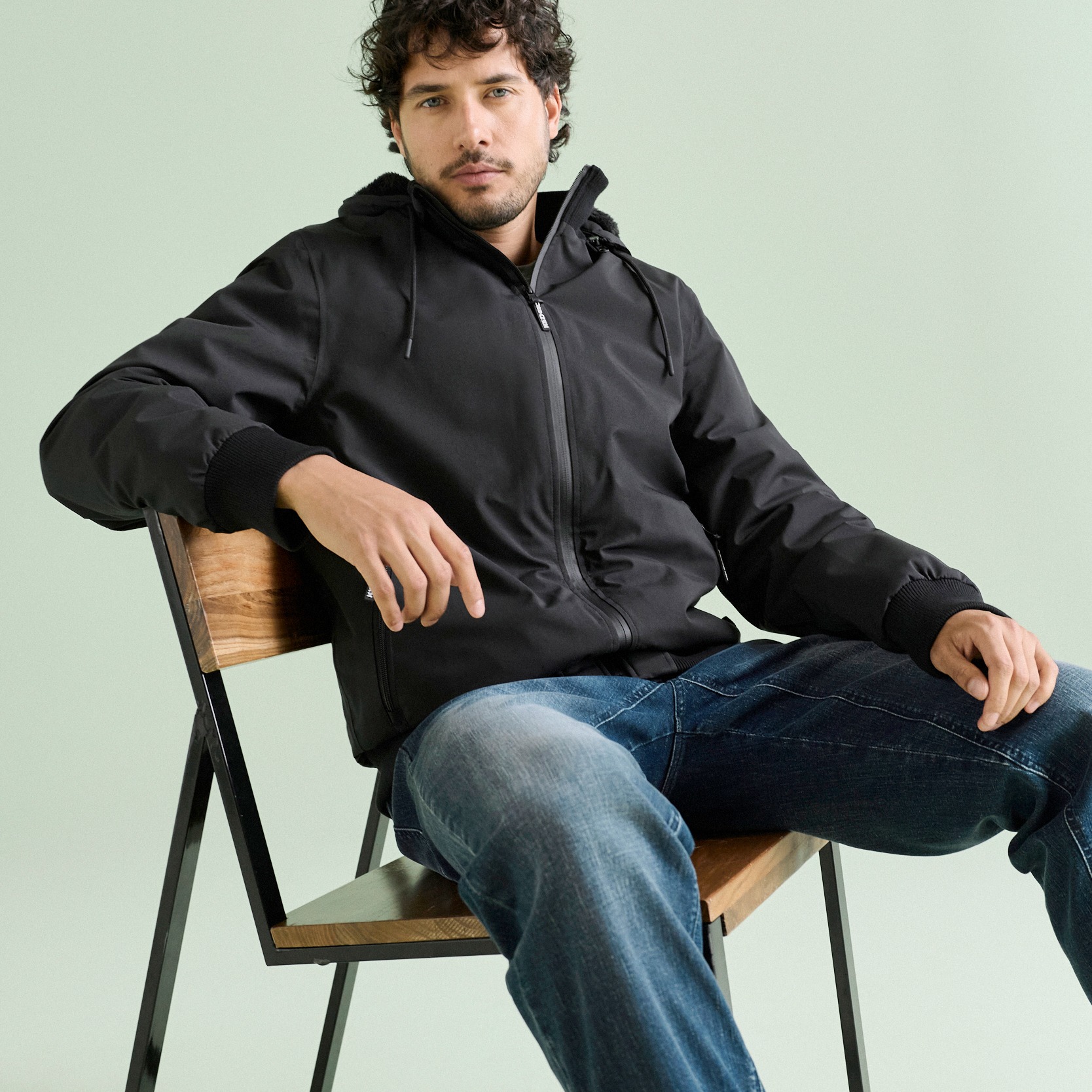 Er trägt eine stilvolle schwarze Kapuzenjacke und bequeme blaue Jeans.