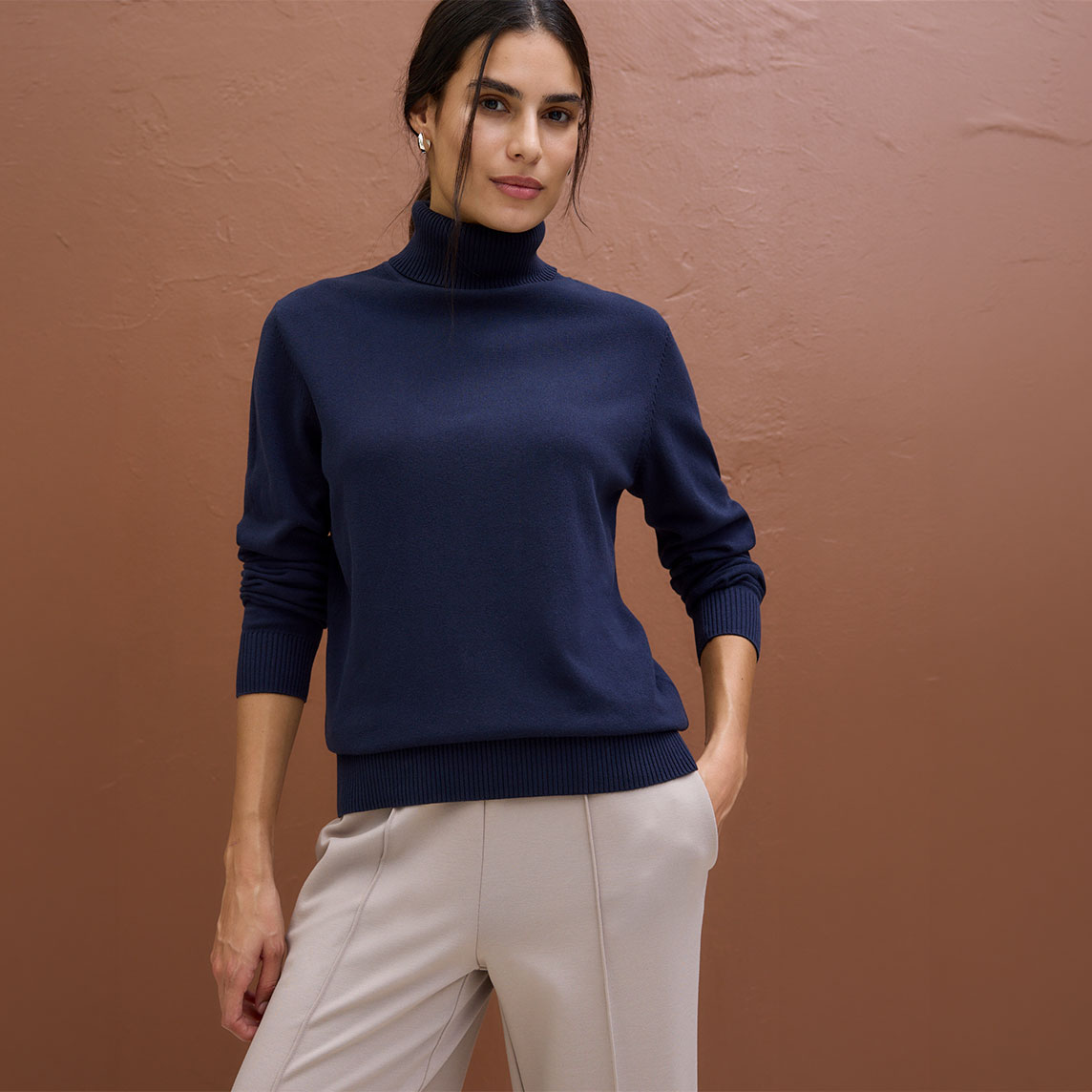 Dunkelblauer Rollkragenpullover und elegante helle Hose bilden ein stilvolles Outfit.