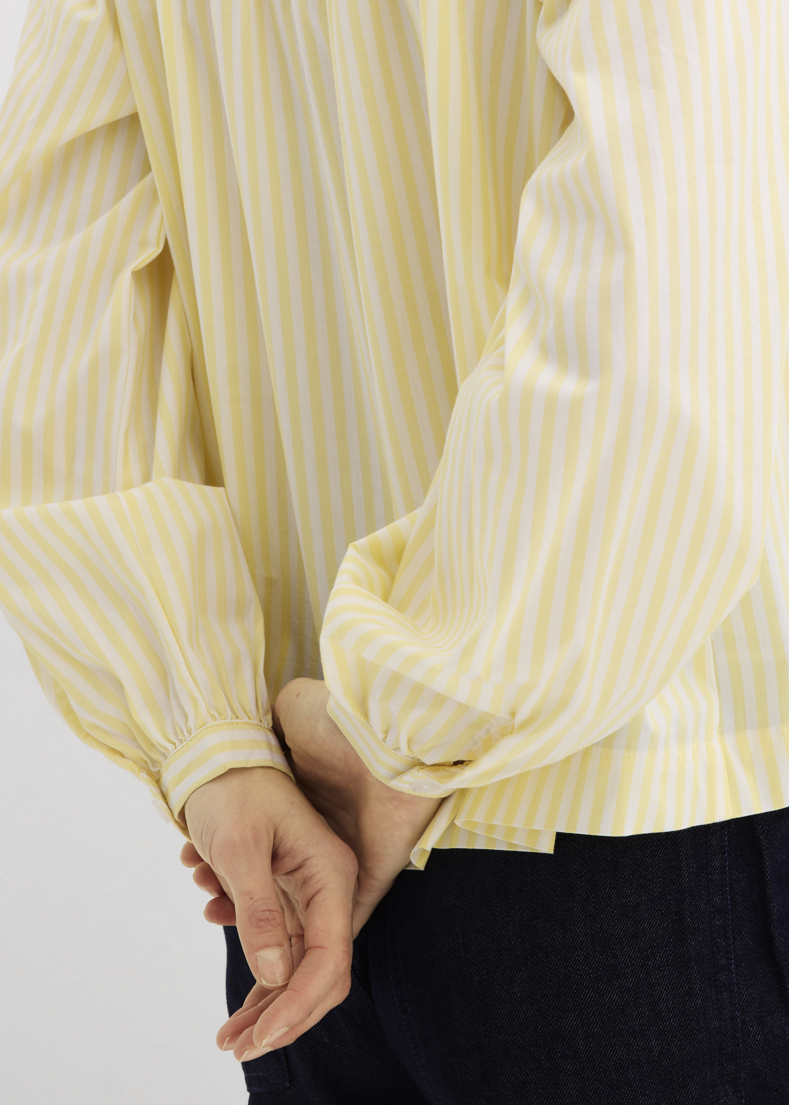 Die gelb-weiß gestreifte Bluse mit bauschigen Ärmeln passt zur dunklen Hose.