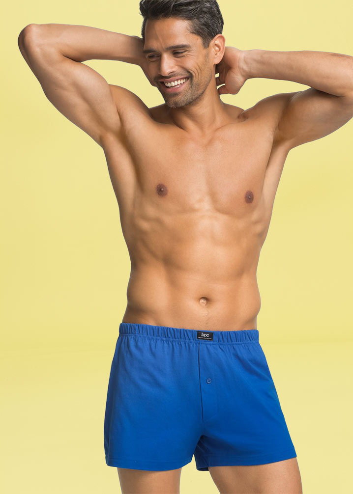 Ein muskulöser Mann trägt blaue Boxershorts.