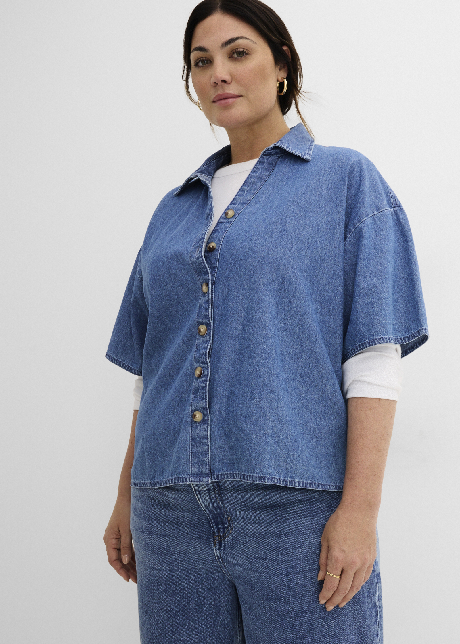 Blaues Oversize-Jeanshemd über weißem Langarmshirt und weite Denim-Hose.