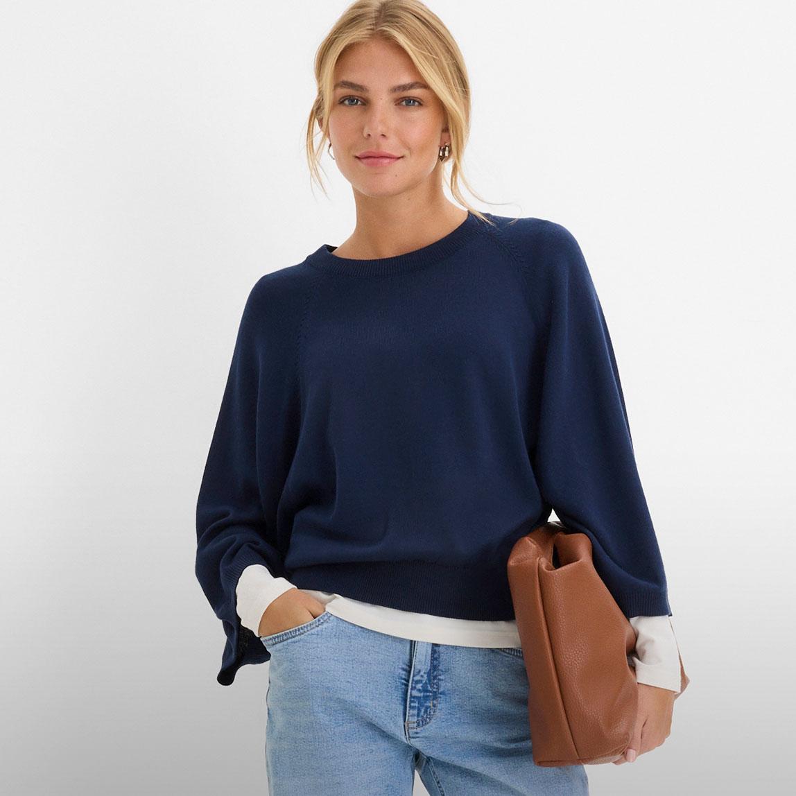 Dunkelblauer Pullover, helle Jeans und eine braune Handtasche.