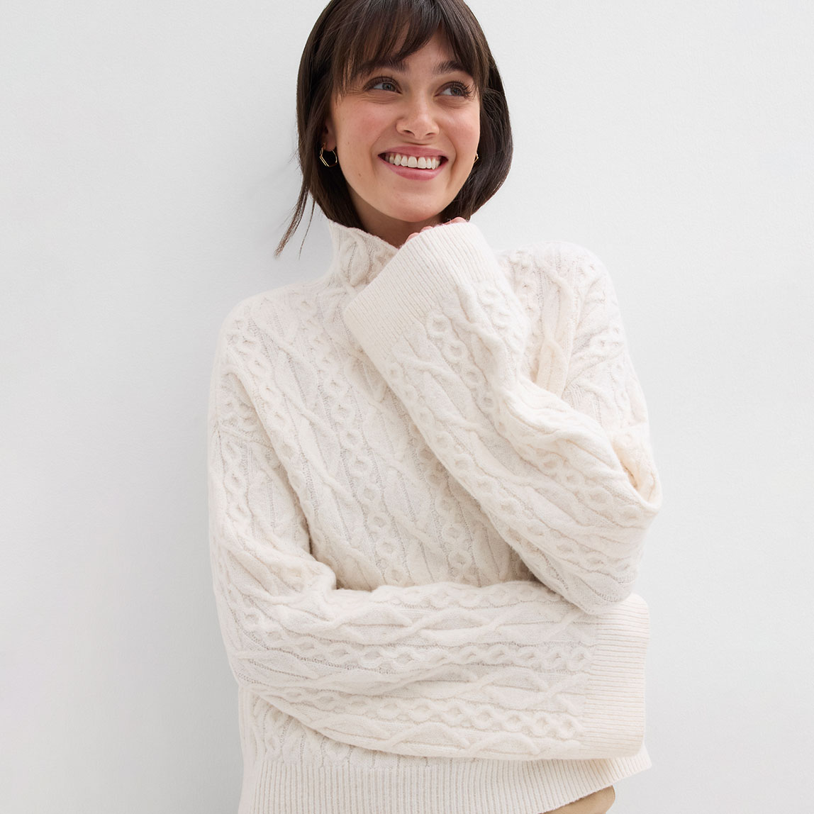 Weißer Strickpullover mit hohem Kragen und strukturiertem Muster.