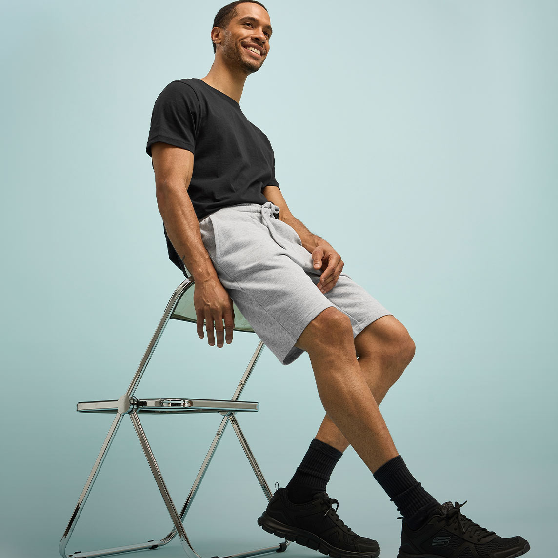Lässiger Look mit schwarzem T-Shirt, heller Shorts und dunklen Sneakers mit Socken.