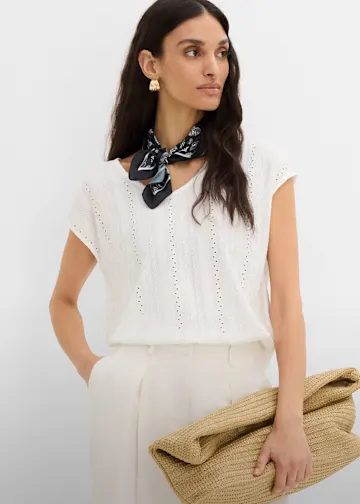 Weiße Shirtbluse mit Lochmuster, helle Hose, dunkles Halstuch und Stroh-Clutch.