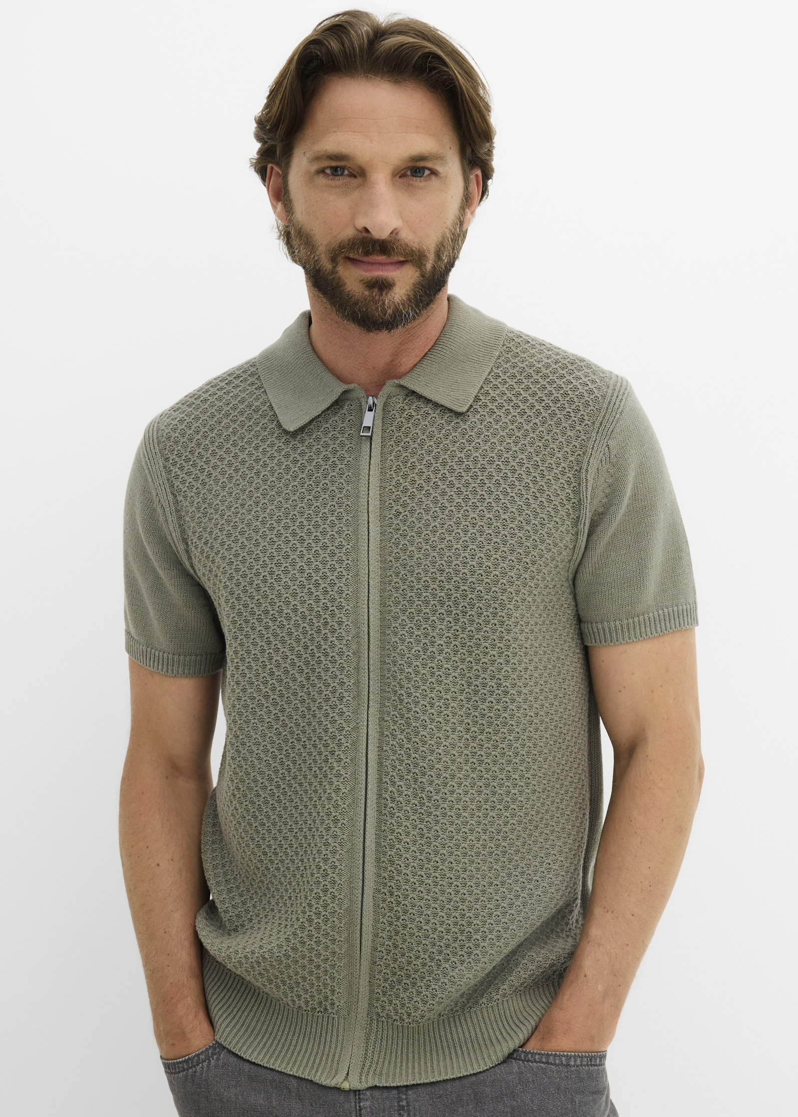 Grünes Strickpolohemd mit Reißverschluss und markantem Muster, kombiniert mit dunkler Jeans.