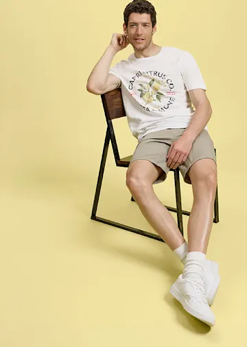 Weißes Capri-Citrus-T-Shirt, beigefarbene Shorts, weiße Socken und Sneaker.