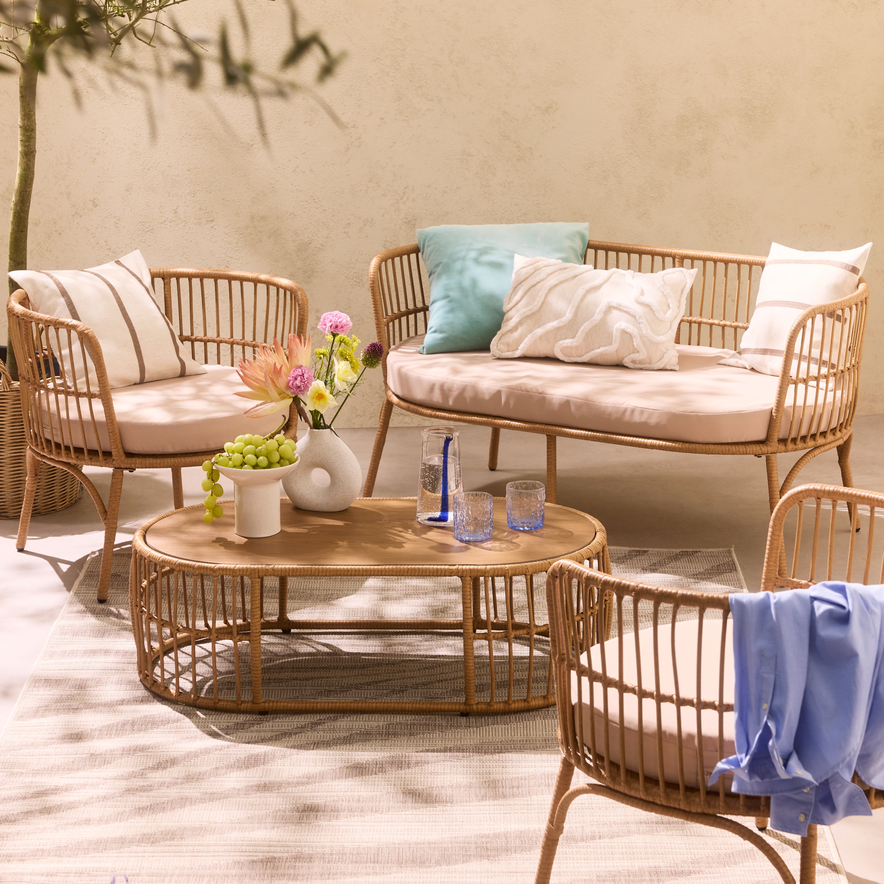 Gemütliche Rattanmöbel mit hellen Kissen und Decken laden zum Entspannen im Freien ein.