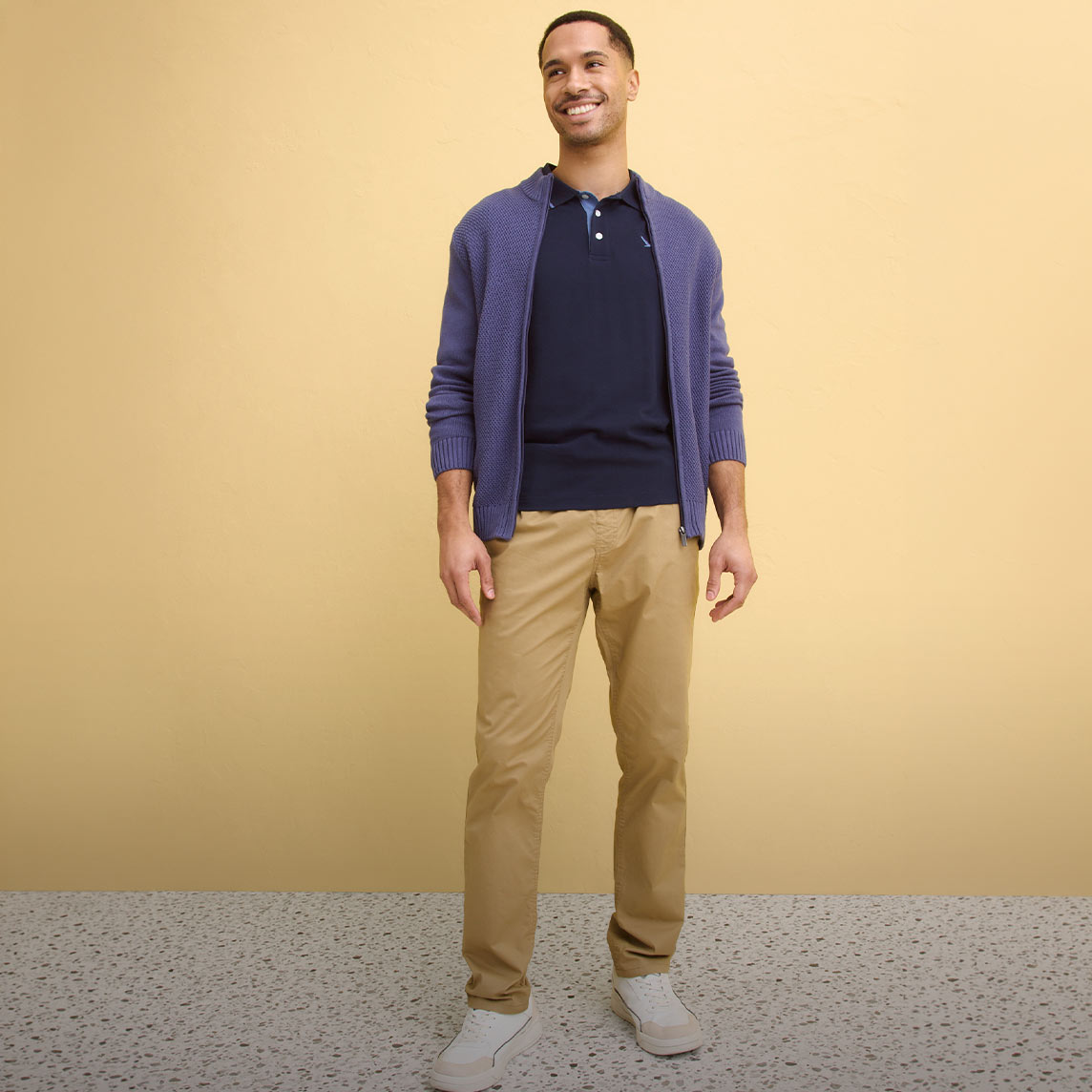 Lila Strickjacke, dunkelblaues Poloshirt, beigefarbene Chinohose, weiße Schuhe.