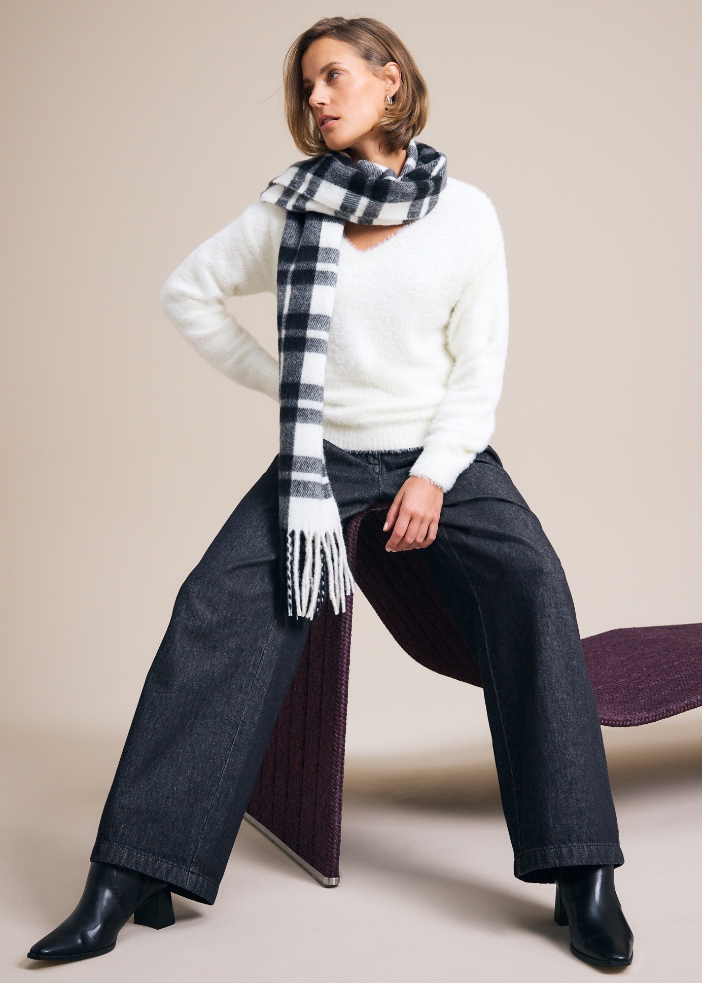 Flauschiger weißer Pullover, karierter Schal, weite dunkle Hose und stylische Stiefeletten.