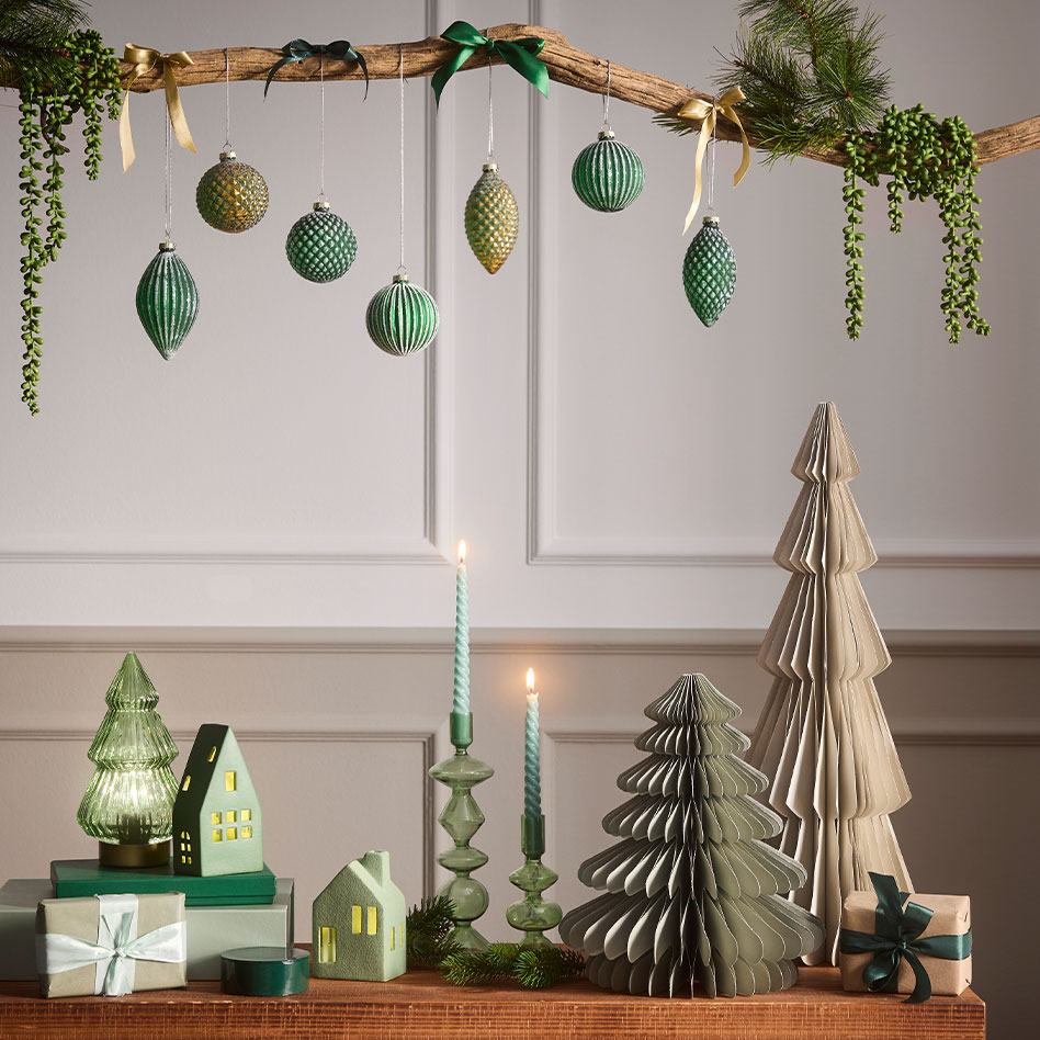 Festliche grüne Weihnachtsdekoration mit hängenden Kugeln, Papierbäumen und leuchtenden Kerzen.