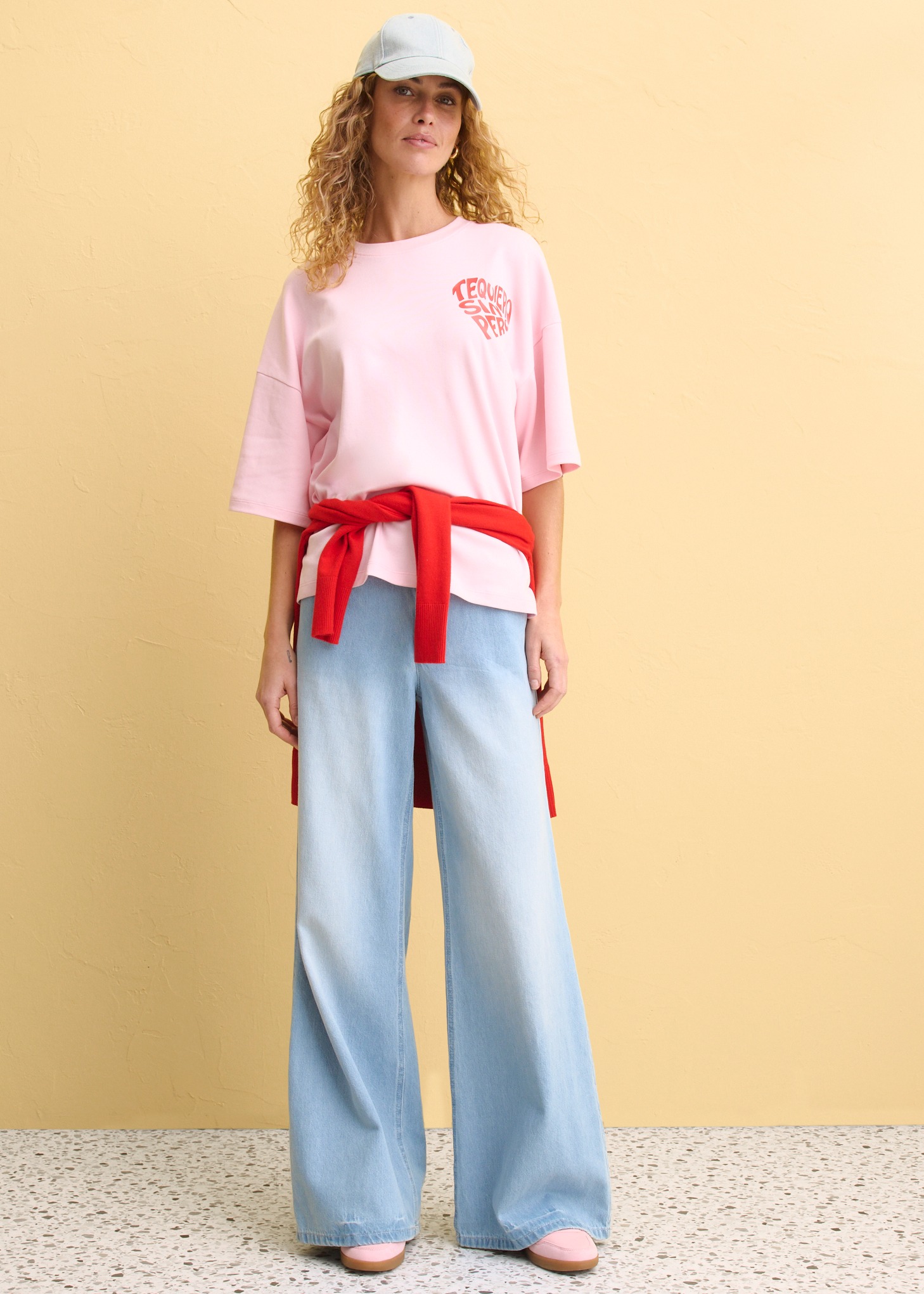 Rosa Oversize-Shirt mit Logo, hellblaue Schlaghose und roter Gürtel. 