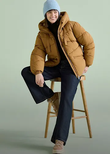 Die Person trägt eine hellblaue Mütze, eine braune Steppjacke und dunkle Jeans.