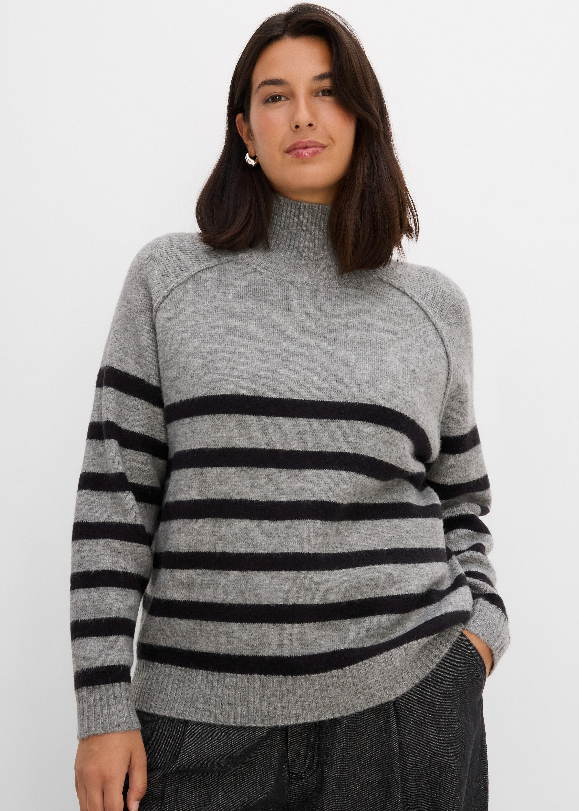 Gestrickter Rollkragenpullover in Grau mit schwarzen Querstreifen und dunkler Hose.