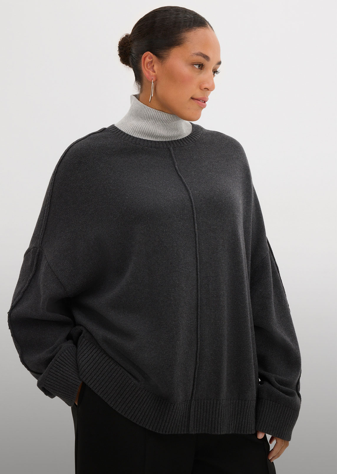 Gemütlicher Oversize-Pullover in Anthrazit über hellem Rollkragen. Lässiger Stil mit sichtbaren Nähten.
