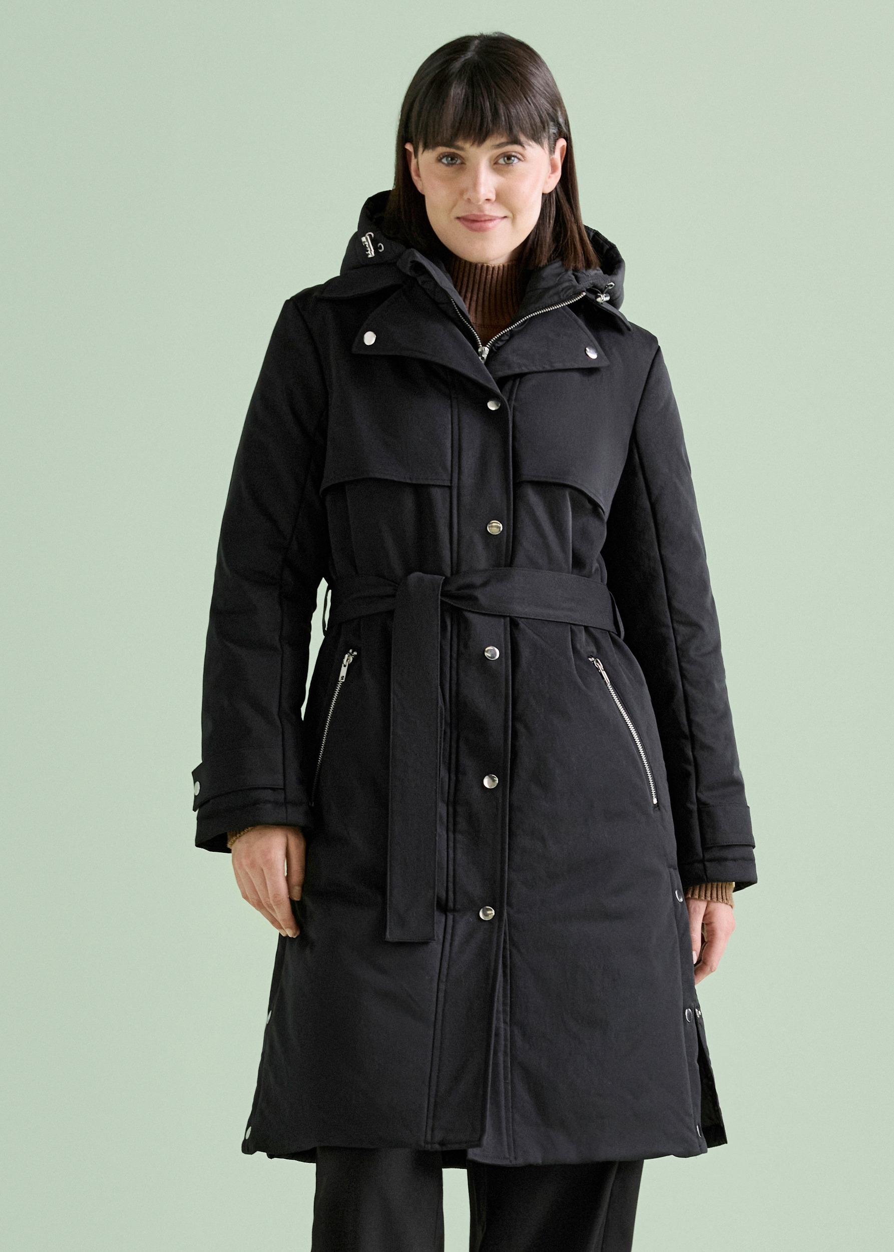 Ein schicker schwarzer Steppmantel mit Kapuze und Gürtel über Hose und Schuhen.