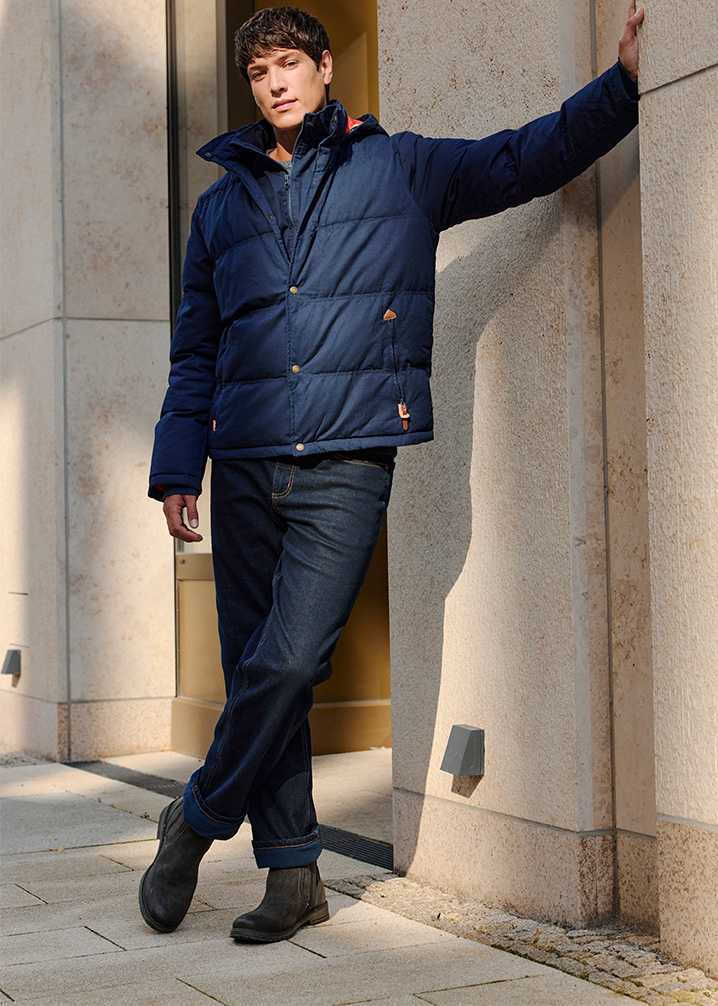 Dunkle Jeans und robuste Stiefel ergänzen die warme Winterjacke.