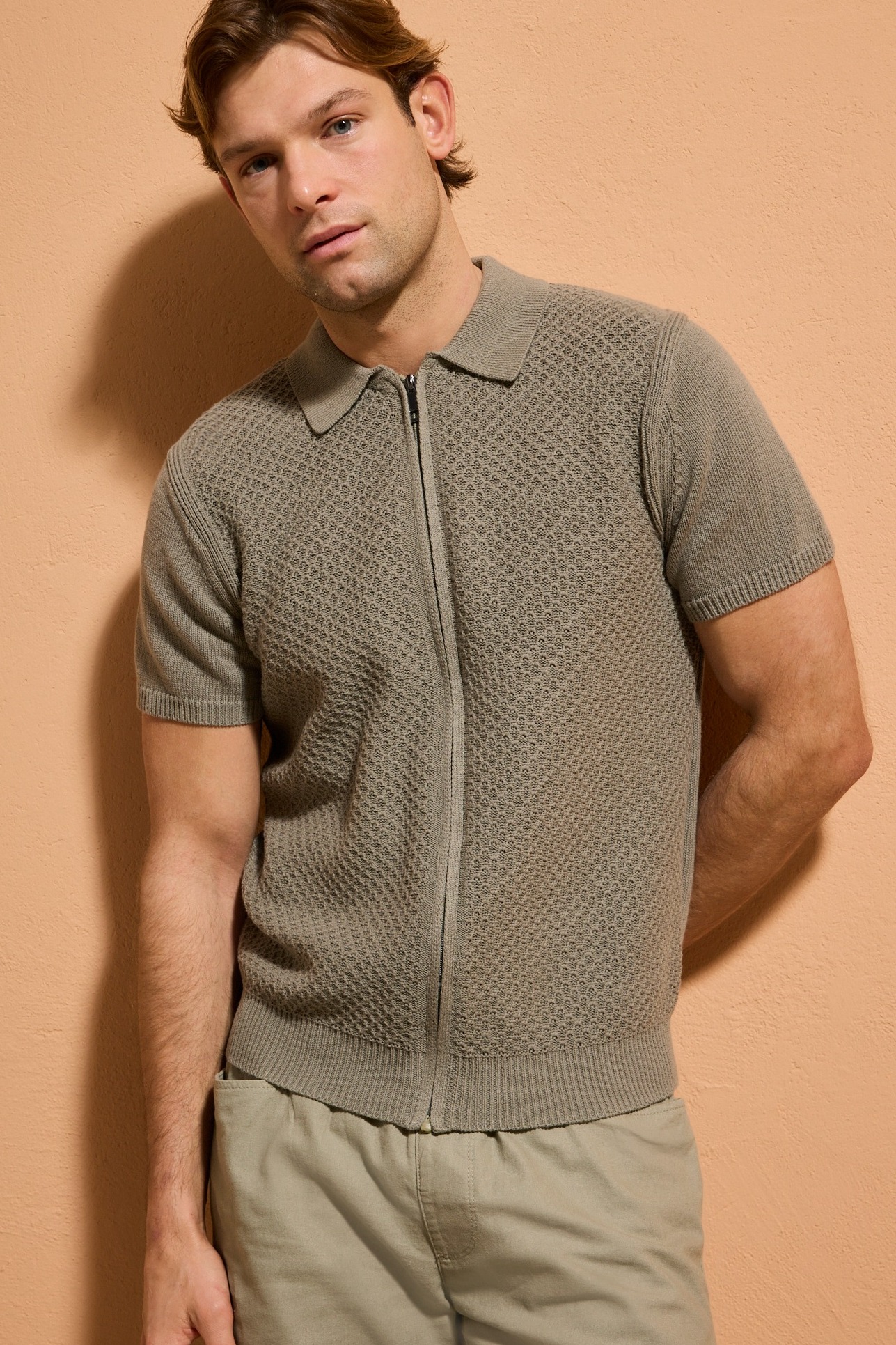 Gestricktes graues Poloshirt mit Reißverschluss und beige Hose.