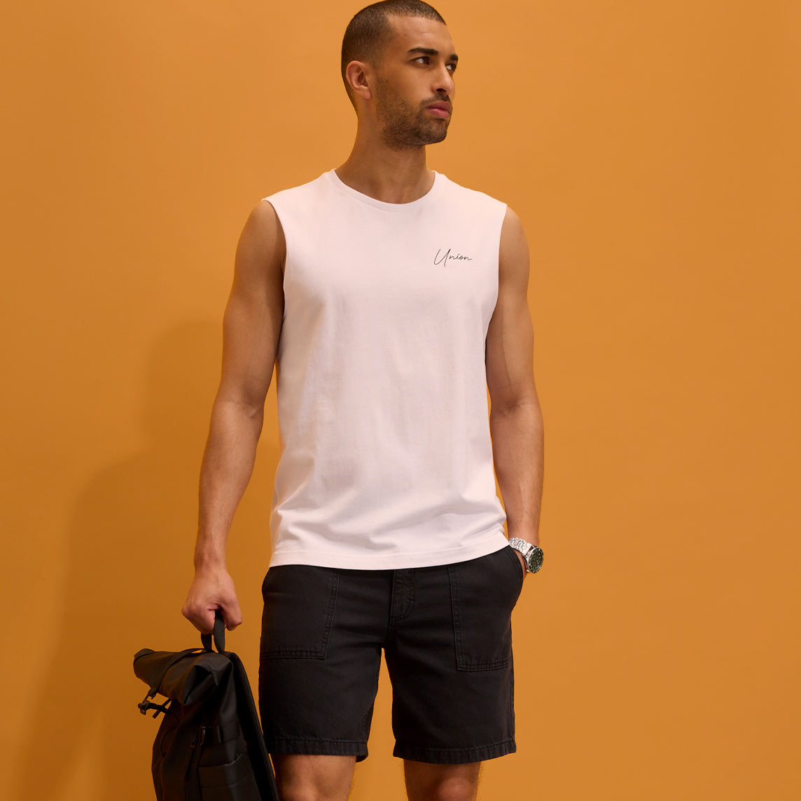 Weißes ärmelloses Shirt, dunkle Shorts und Armbanduhr.