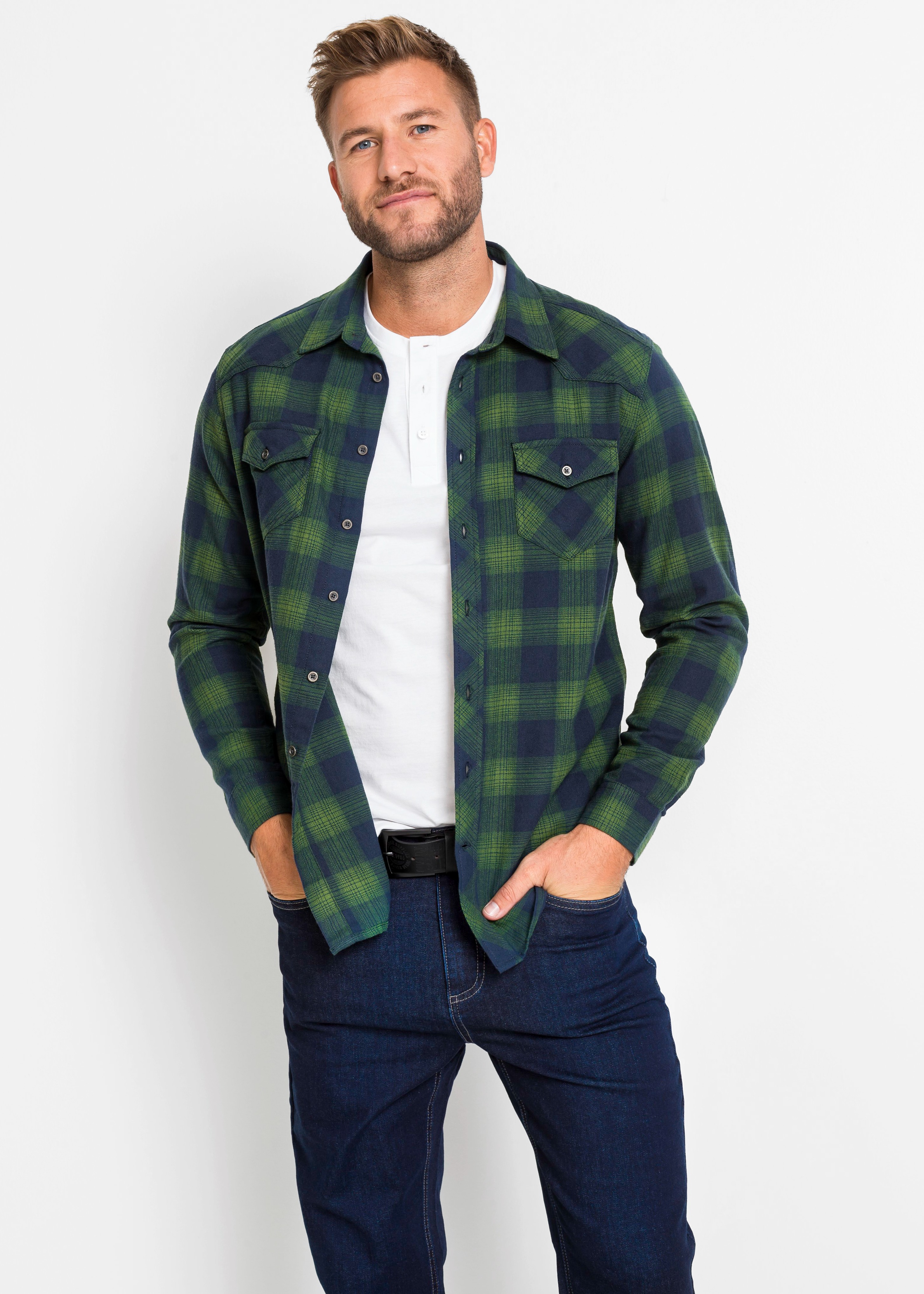Grün-blaues Karomuster-Hemd, weißes Henley-Shirt, dunkle Jeans und schwarzer Gürtel bilden das Outfit.
